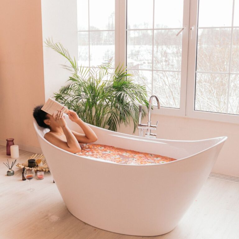 Mujer leyendo en una bañera de cerámica llena de agua con pétalos de rosa